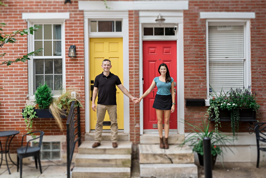 A newly engaged couple hold hands in front of a yellow & red door in Philly.